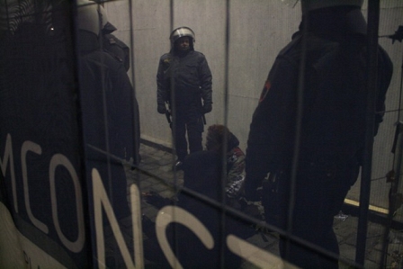 Demonstrant hinter einem Zaun auf dem Boden sitzend, umgeben von Polizisten